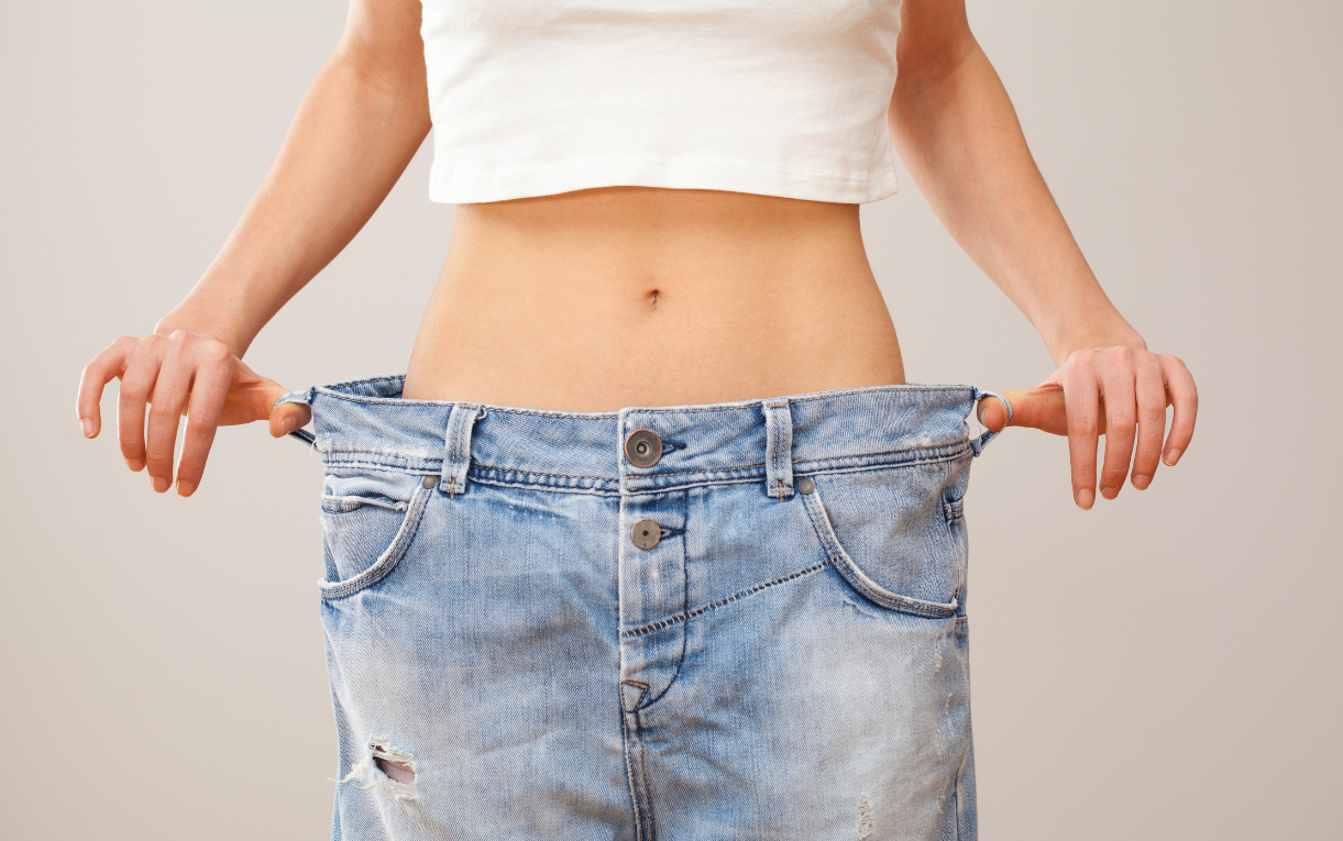 Person in a white crop top holds out oversized jeans at the waist to show a loose fit of the jeans.